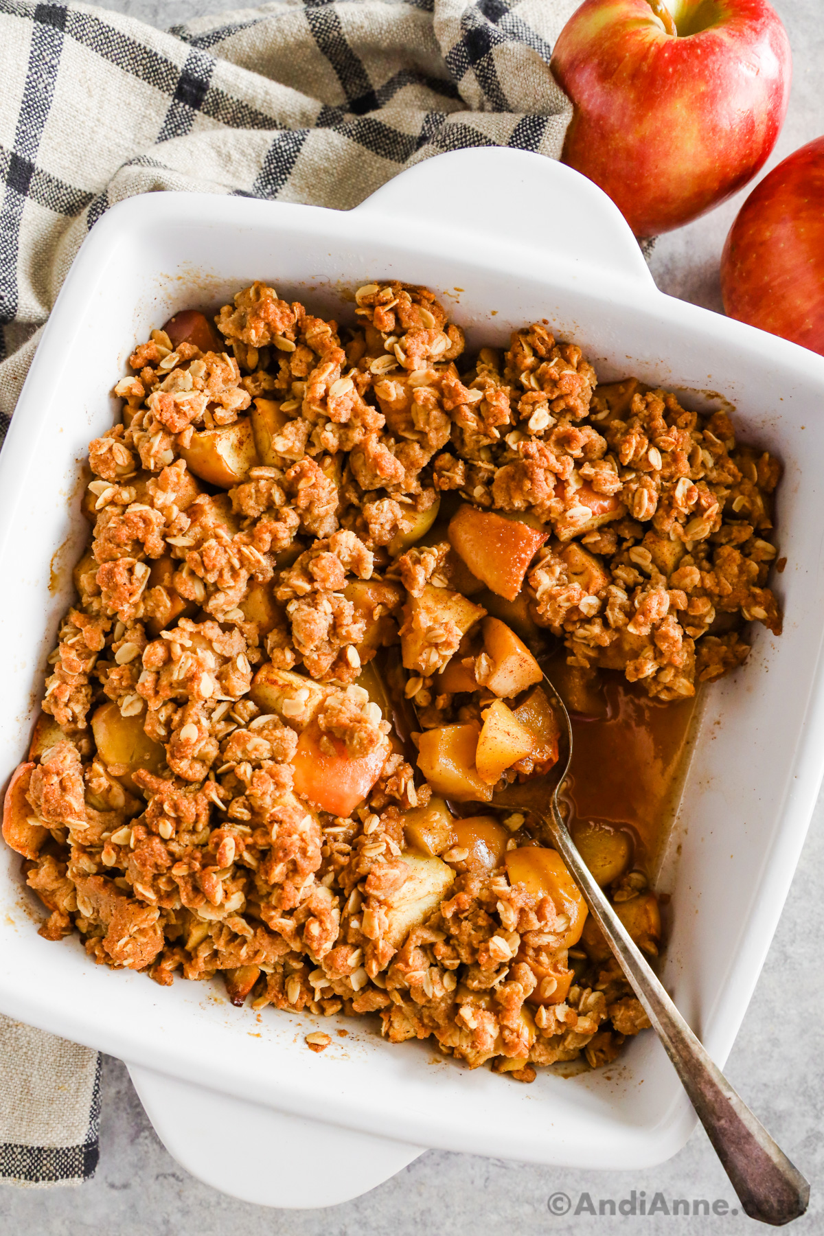 A white baking dish with apple crisp recipe and a spoon.