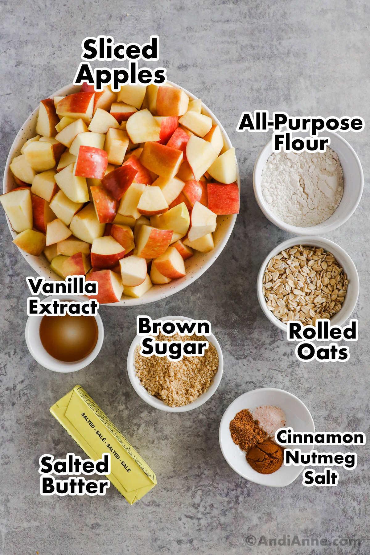 Recipe ingredients including bowls of chopped apples, all purpose flour, rolled oats, brown sugar, vanilla, spices and a stick of butter.
