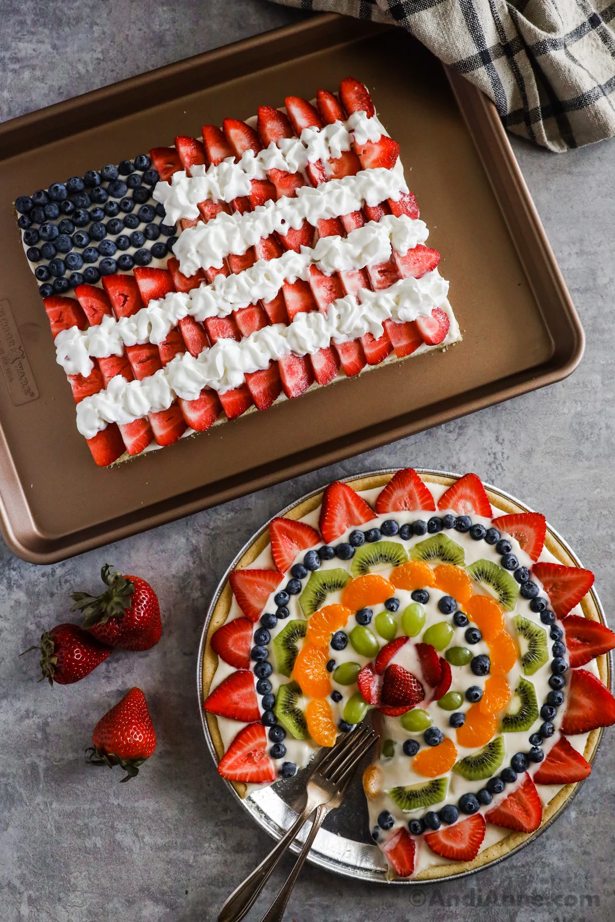two fruit pizzas, one in the shape of a an American flag, the other in a round shape with colorful fruits and a slice cut out.