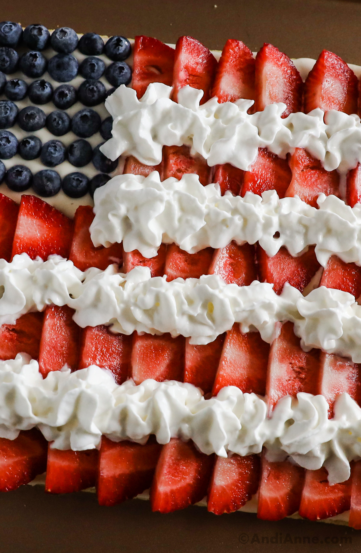 Close up of blueberries, sliced strawberries and whipped cream on flag fruit pizza.