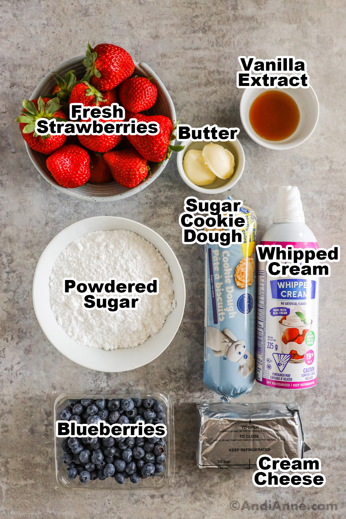 Recipe ingredients including bowl if strawberries, vanilla extract, butter, powdered sugar, sugar cookie dough, whipped cream, blueberries and cream cheese. 