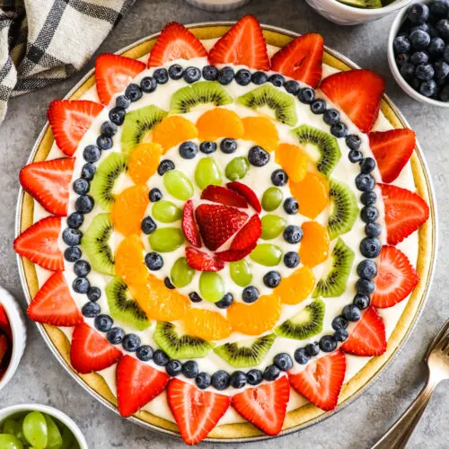 A sugar cookie crust fruit pizza with bowls of fruit beside it.