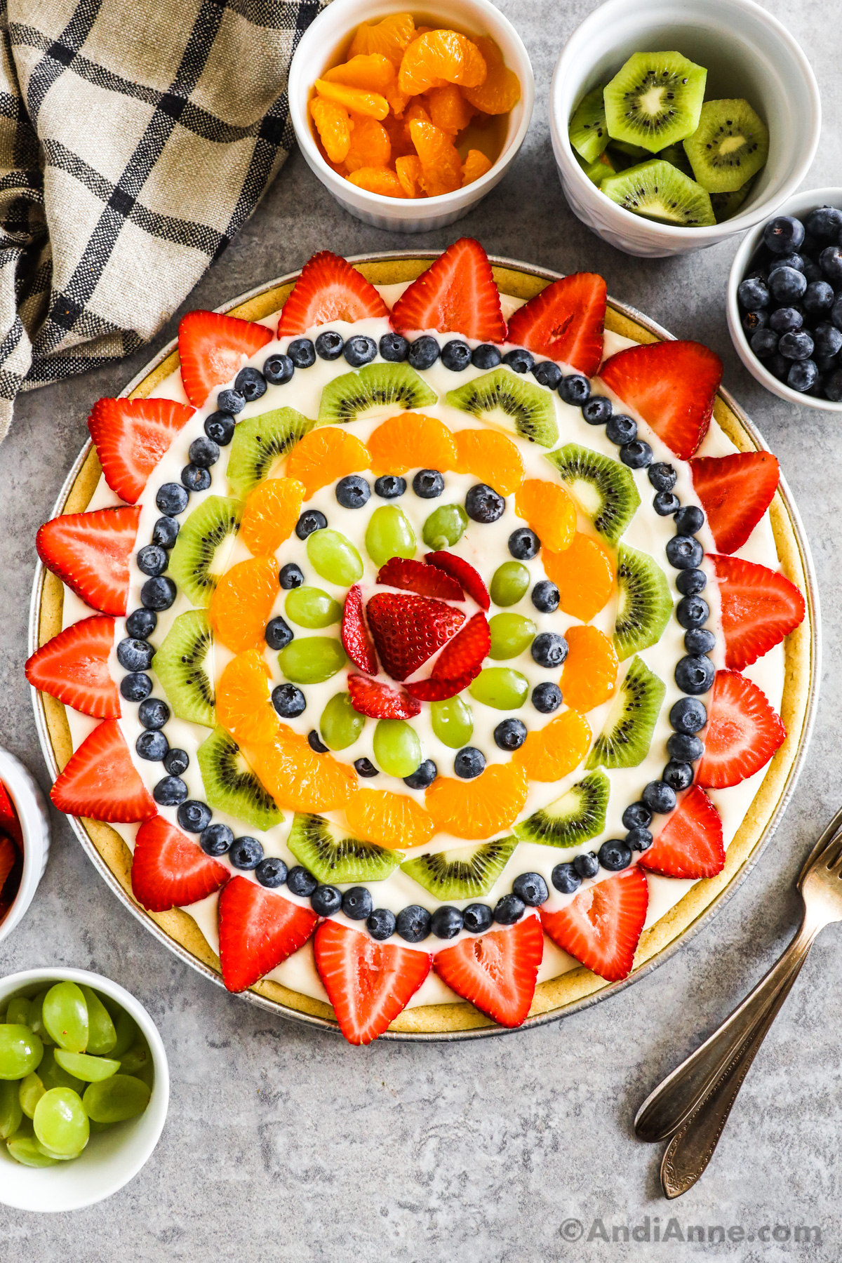 A sugar cookie crust fruit pizza with bowls of fruit beside it.