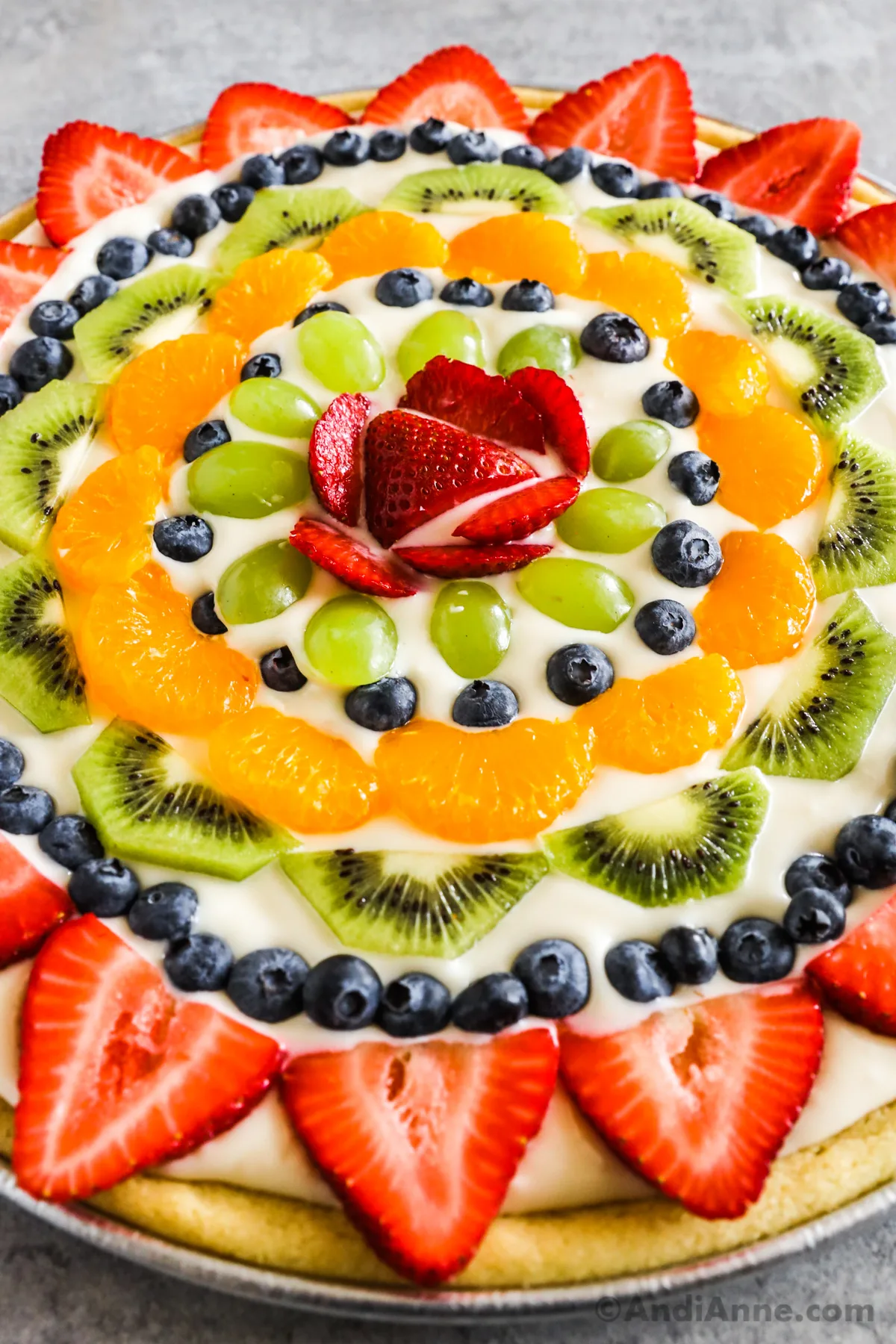 Close up of a fruit pizza with sliced strawberries, kiwis, blueberries, and grapes.