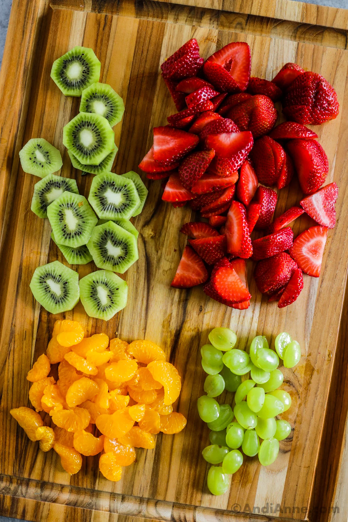 Sliced kiwi, sliced strawberries, sliced grapes and mandarin orange sections on a cutting board.