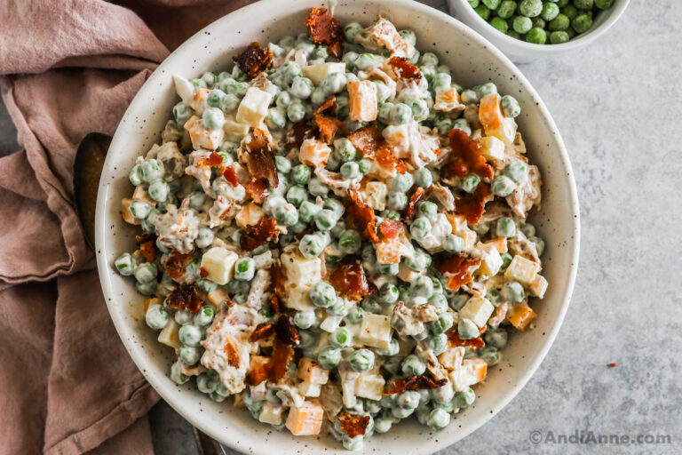 A large bowl of creamy pea salad with bacon pieces sprinkled on top.