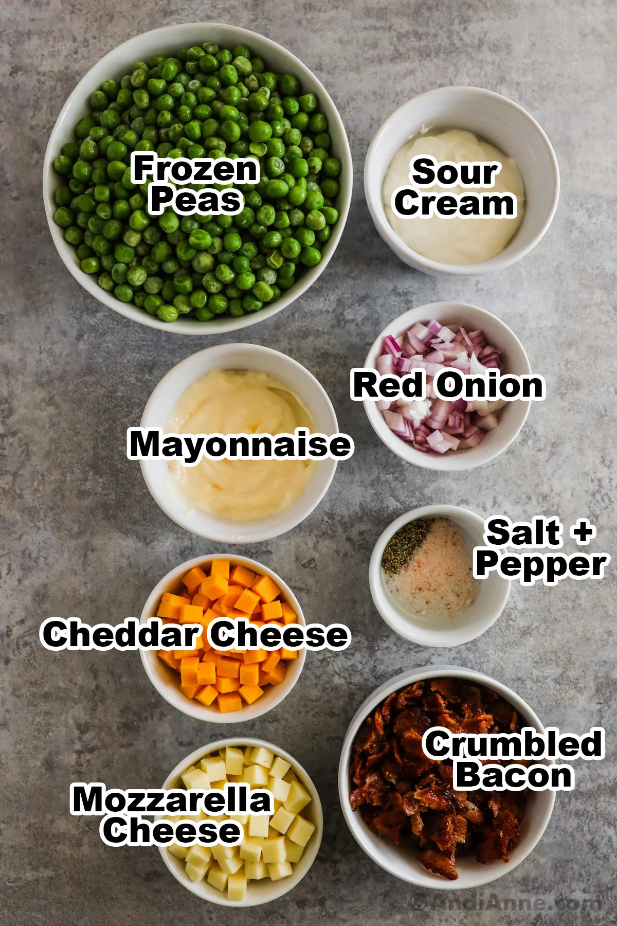 Recipe ingredients in bowls including frozen peas, sour cream, mayonnaise, red onion, cheese, crumbled bacon, salt and pepper.