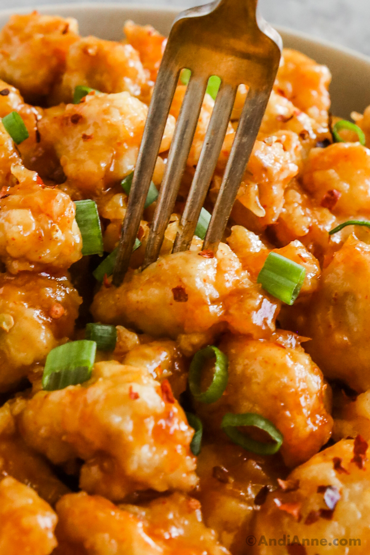Close up of crispy orange chicken with a fork and chopped green onions.