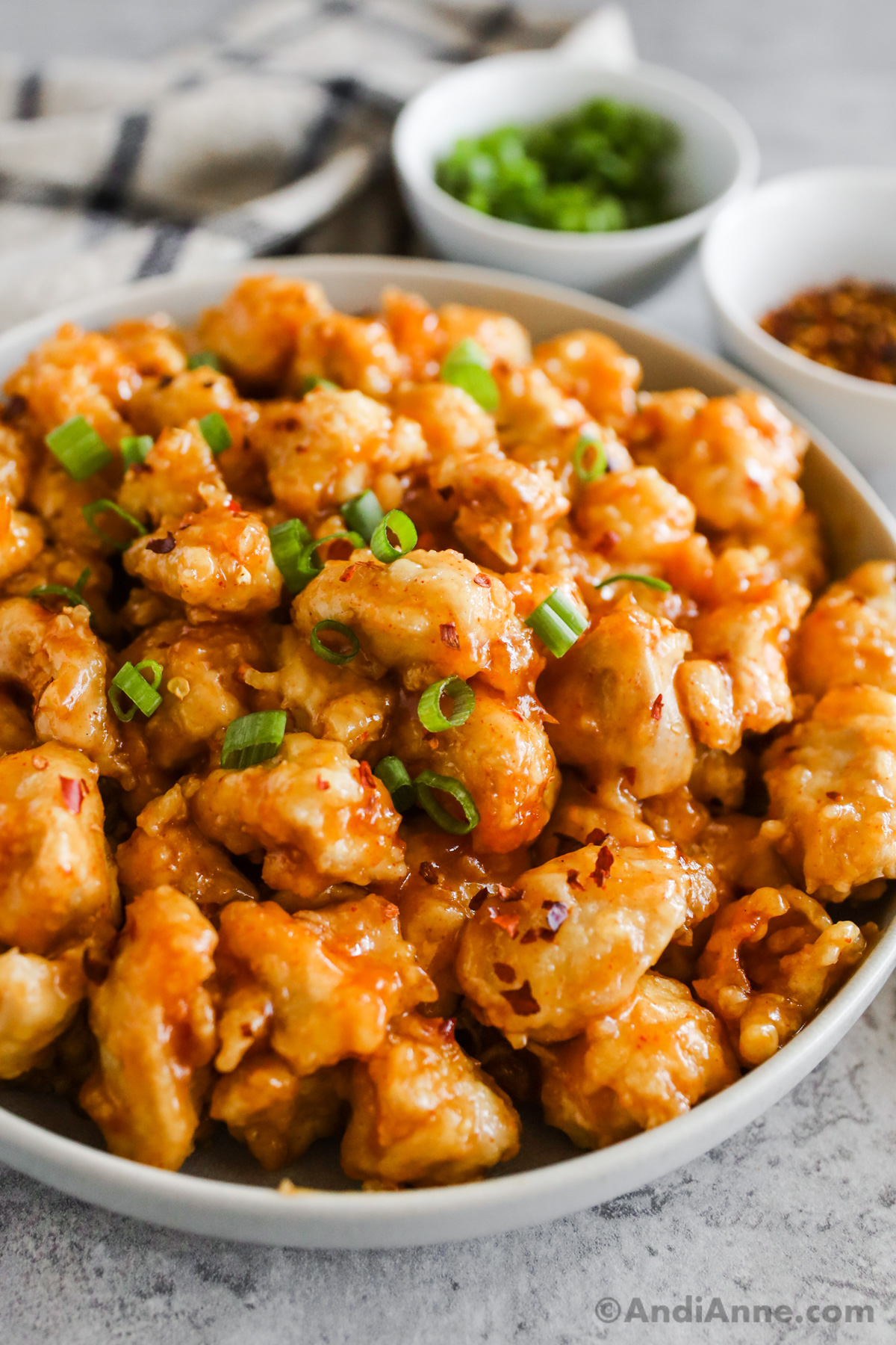 Close up of orange chicken pieces topped with chopped green onion.