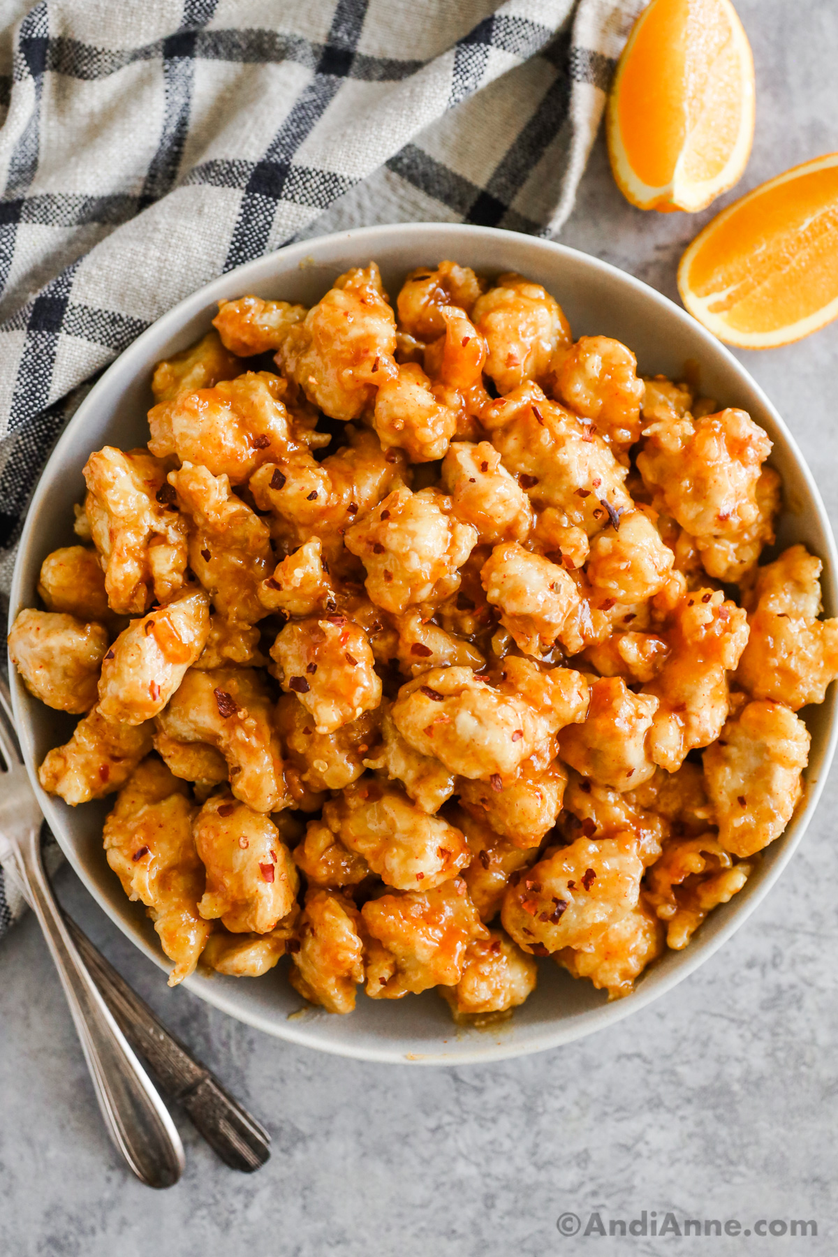 A plate of orange chicken bites covered in sauce and sprinkled with red pepper flakes.