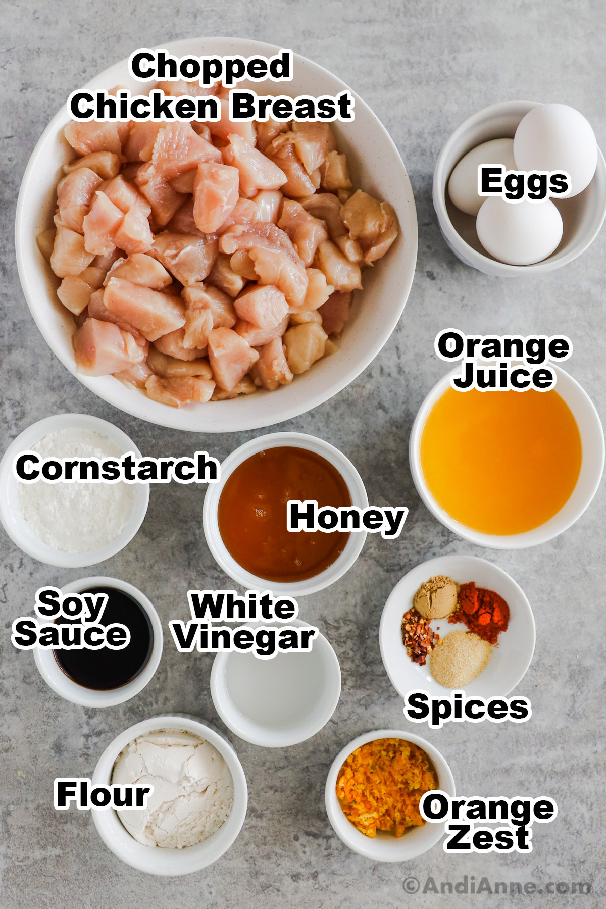 Recipe ingredients on counter in bowls including chopped chicken, eggs, cornstarch, orange juice, honey, soy sauce, white vinegar, flour and orange zest.