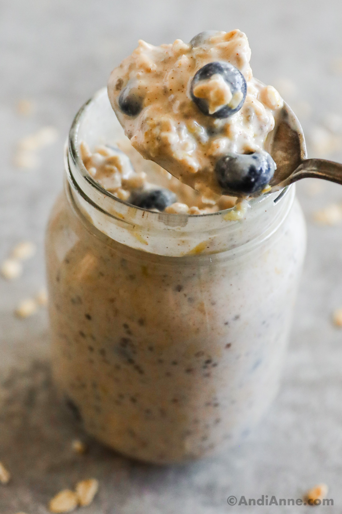 A spoon with blueberry overnight oats and a mason jar with the rest of the overnight oats.
