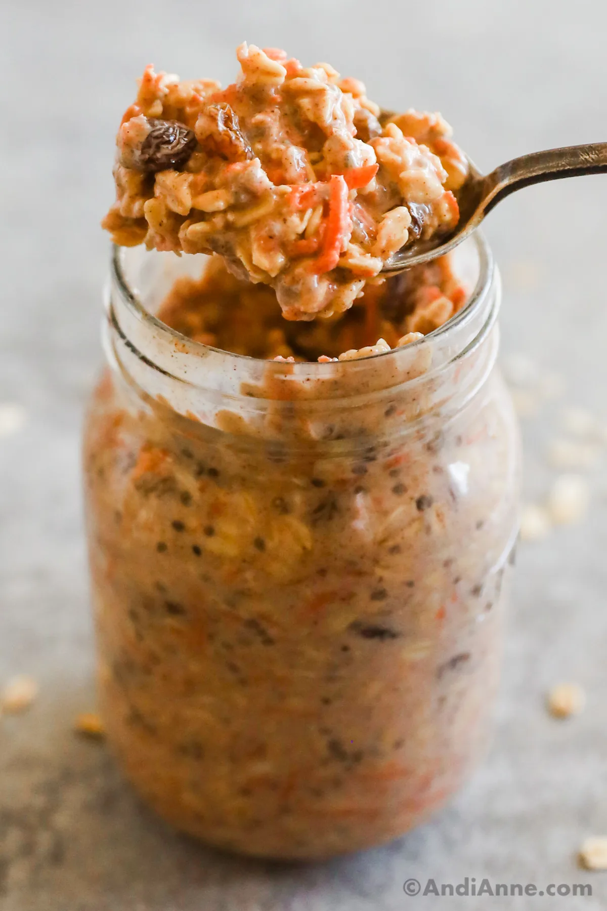A spoon of carrot cake overnight oats overtop of a mason jar with more oats.
