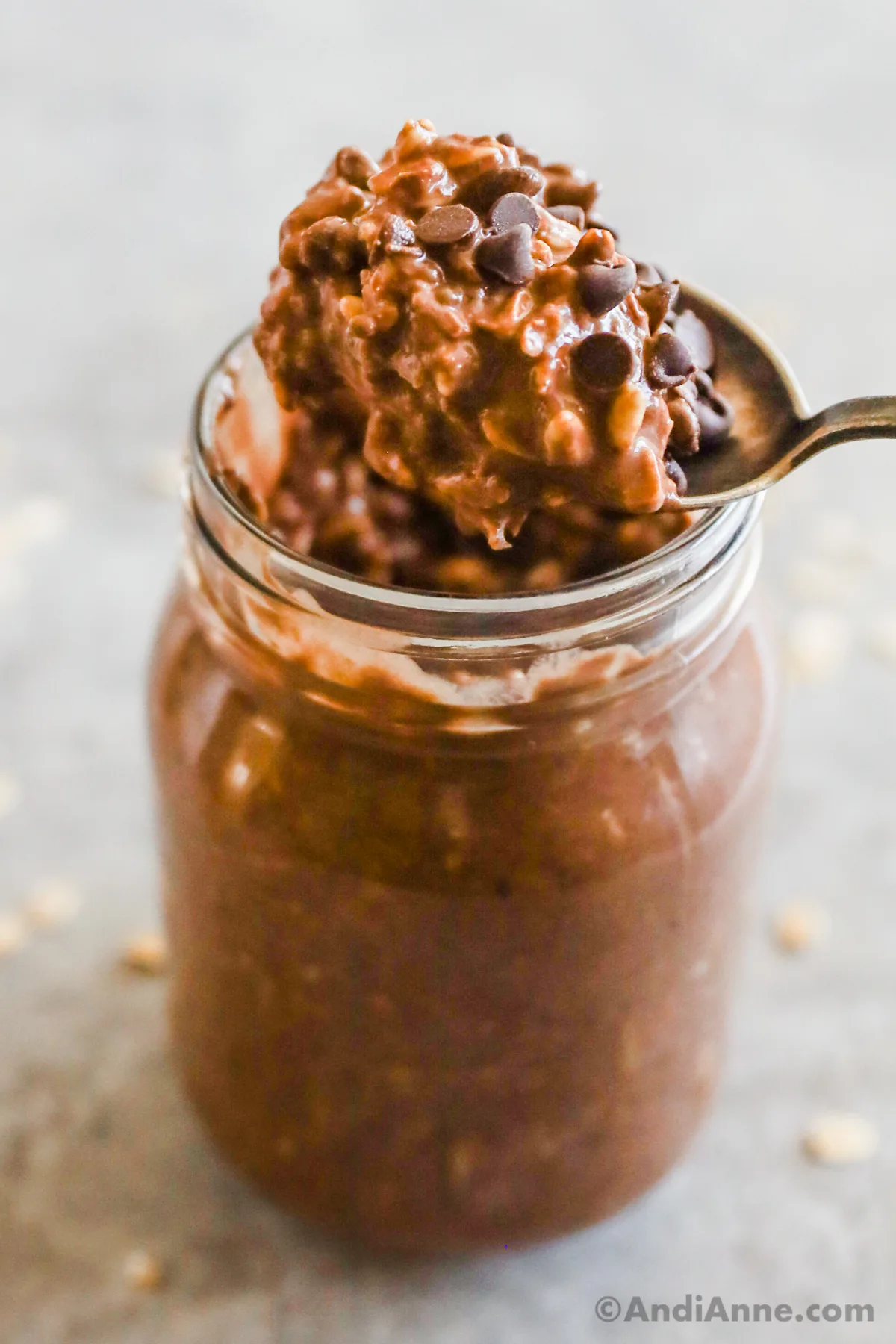 A spoon scooping chocolate overnight oats topped with chocolate chips out of a mason jar.