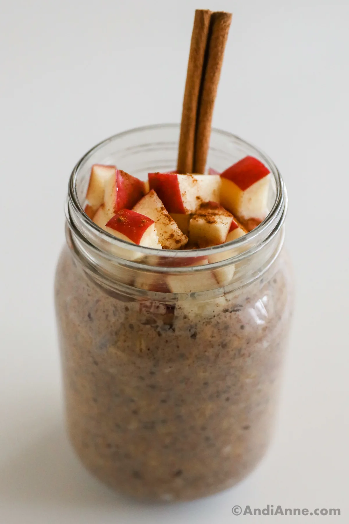 Photo of finished overnight oats with chopped apple and cinnamon stick inside. 