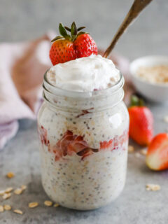 A mason jar with strawberry cheesecake overnight oats, topped with yogurt and a strawberry.