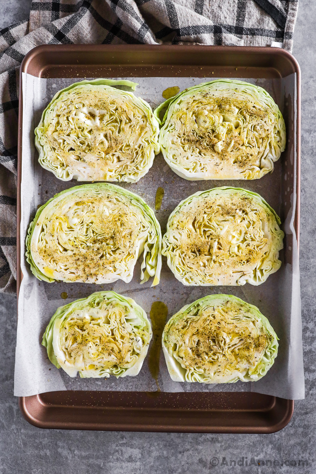 Sliced raw green cabbage on a baking sheet, sprinkled with oil and spices.
