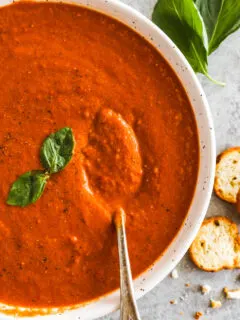 A bowl of roasted tomato basil soup, topped with fresh basil garnish.