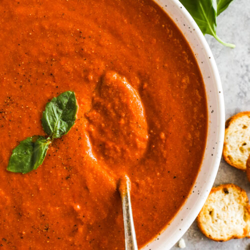 A bowl of roasted tomato basil soup, topped with fresh basil garnish.