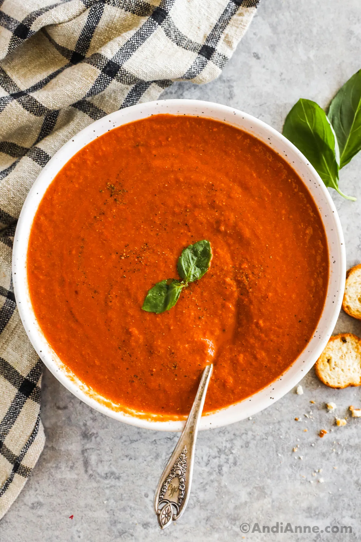 A bowl of roasted tomato basil soup garnished with fresh basil and crackers beside the bowl.
