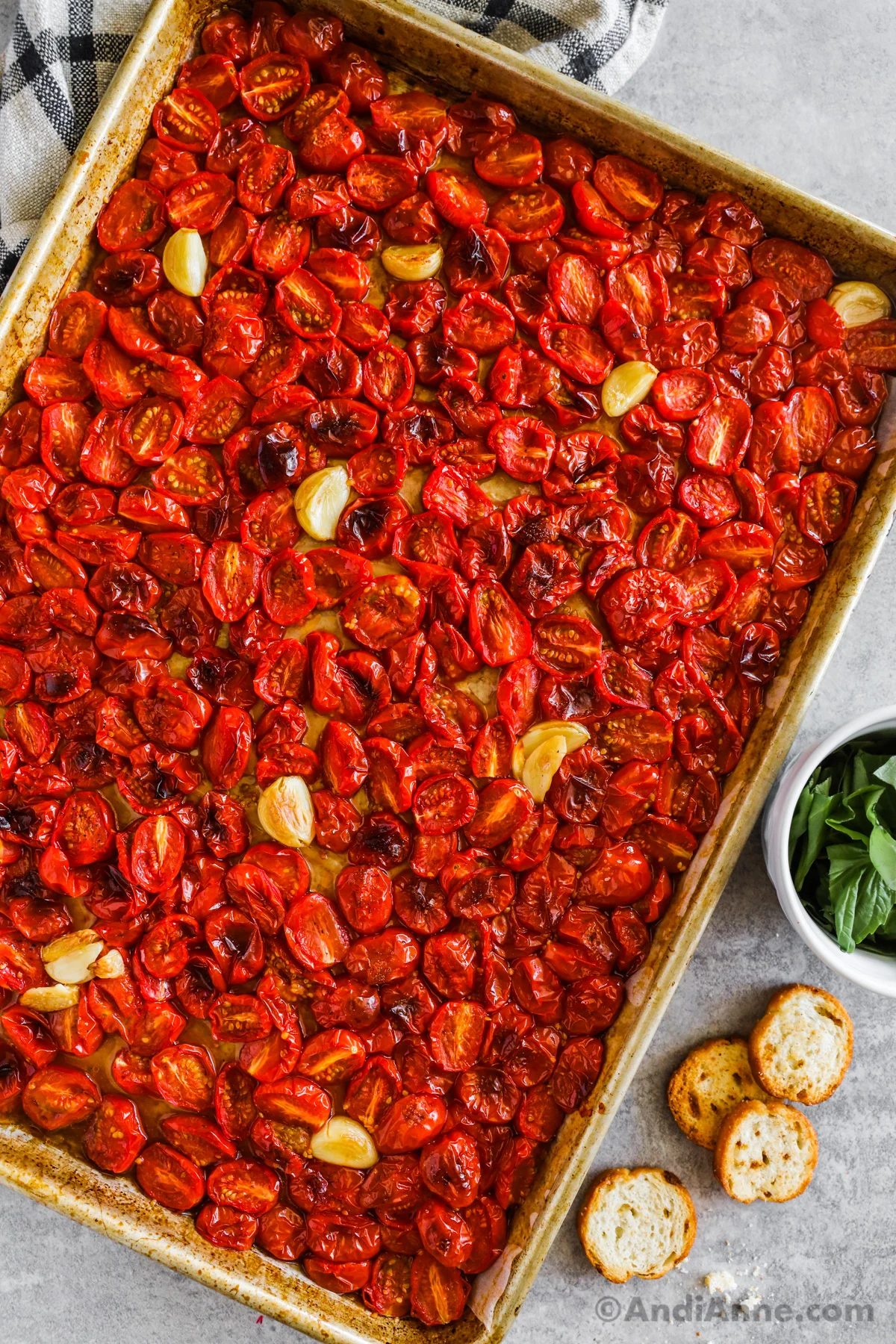 Roasted tomatoes and garlic bulbs on a baking sheet.