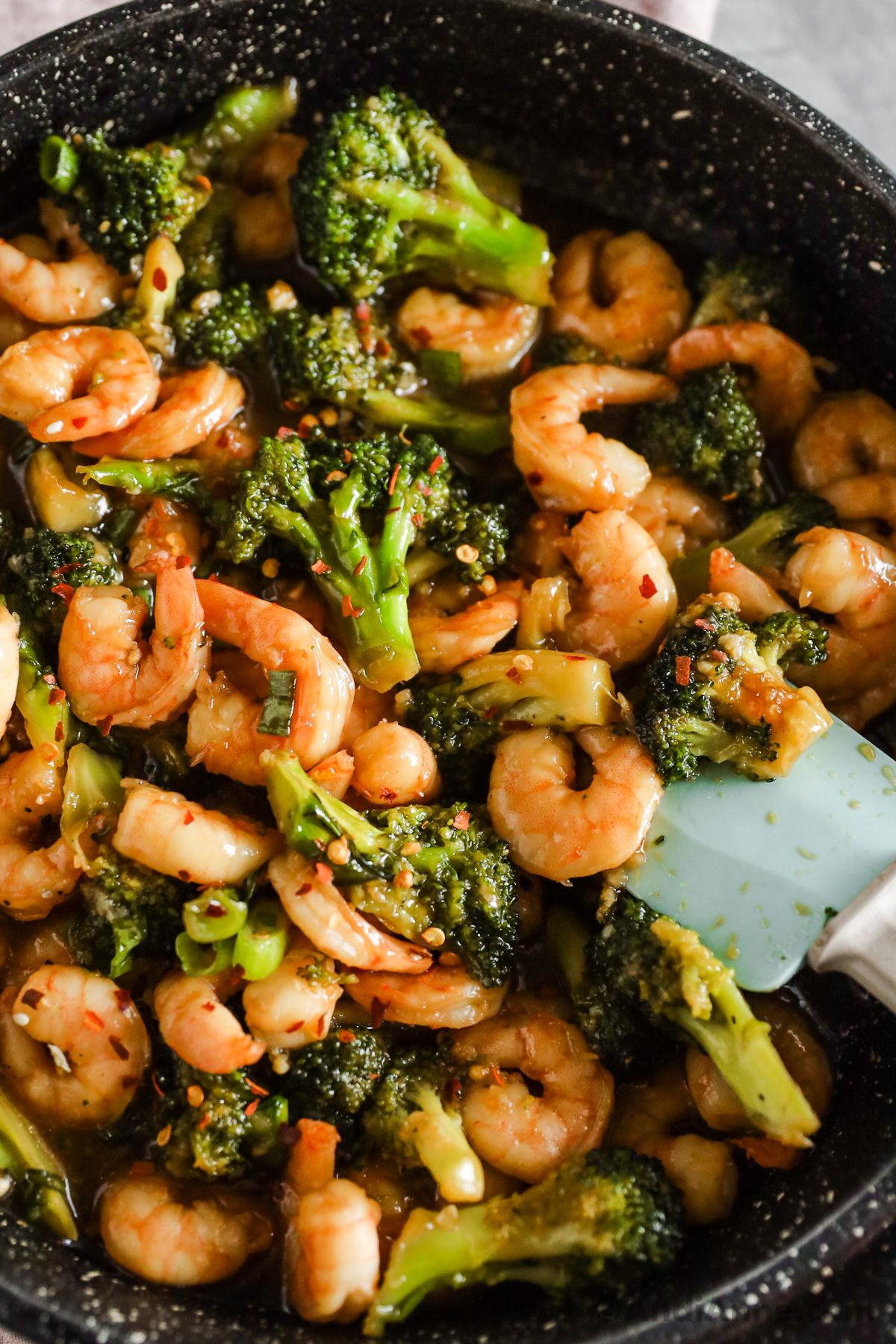 Chopped broccoli florets and shrimp in a sauce with red pepper flakes sprinkled on top. 