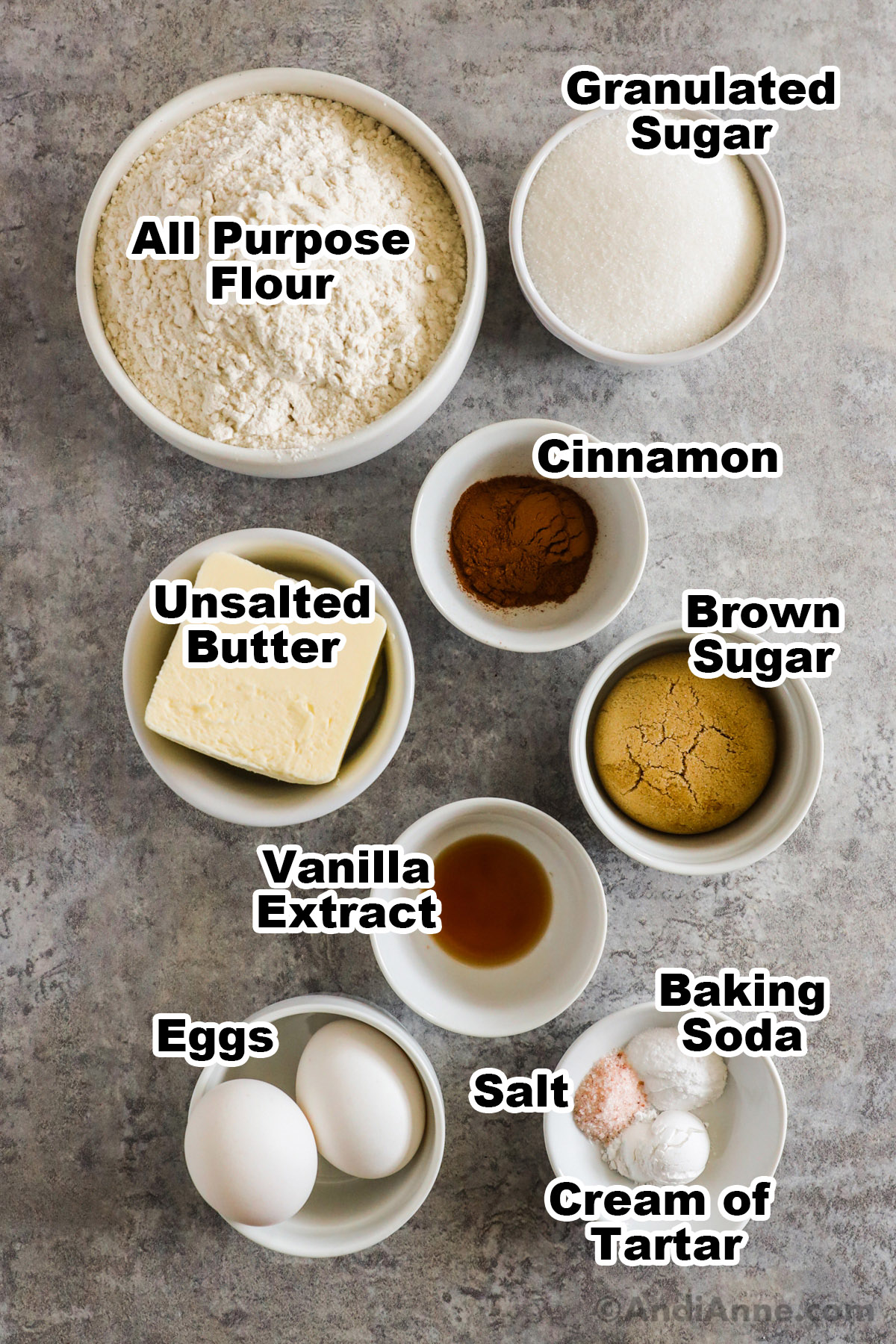 Recipe ingredients on the counter including bowls of flour, sugar, butter, cinnamon, brown sugar, vanilla, eggs, baking soda, salt and cream of tartar.