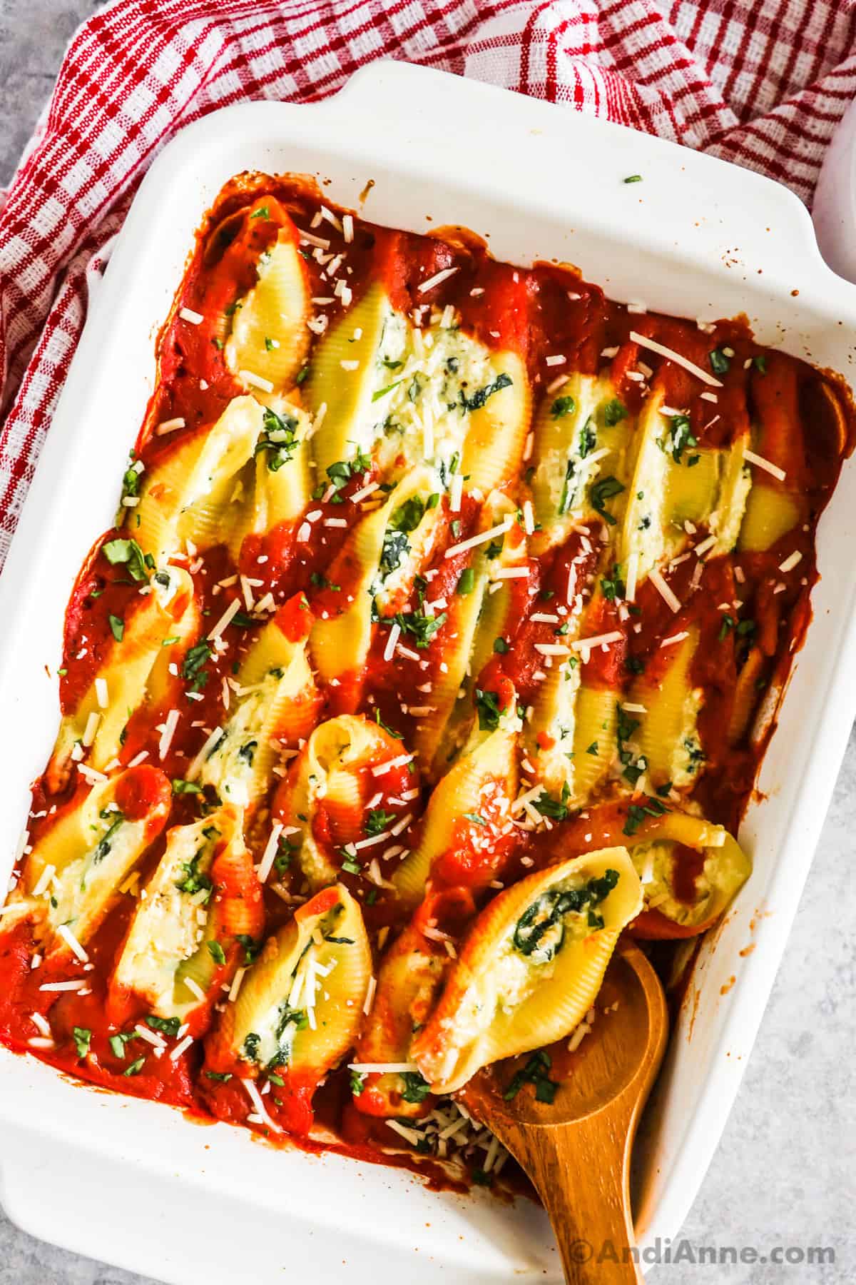 spinach ricotta stuffed shells stacked in a single layer and covered in marinara sauce, all in a white baking dish.