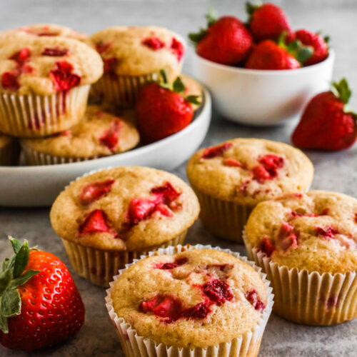 A bunch of fresh strawberry muffins with a bowl of fresh strawberries.