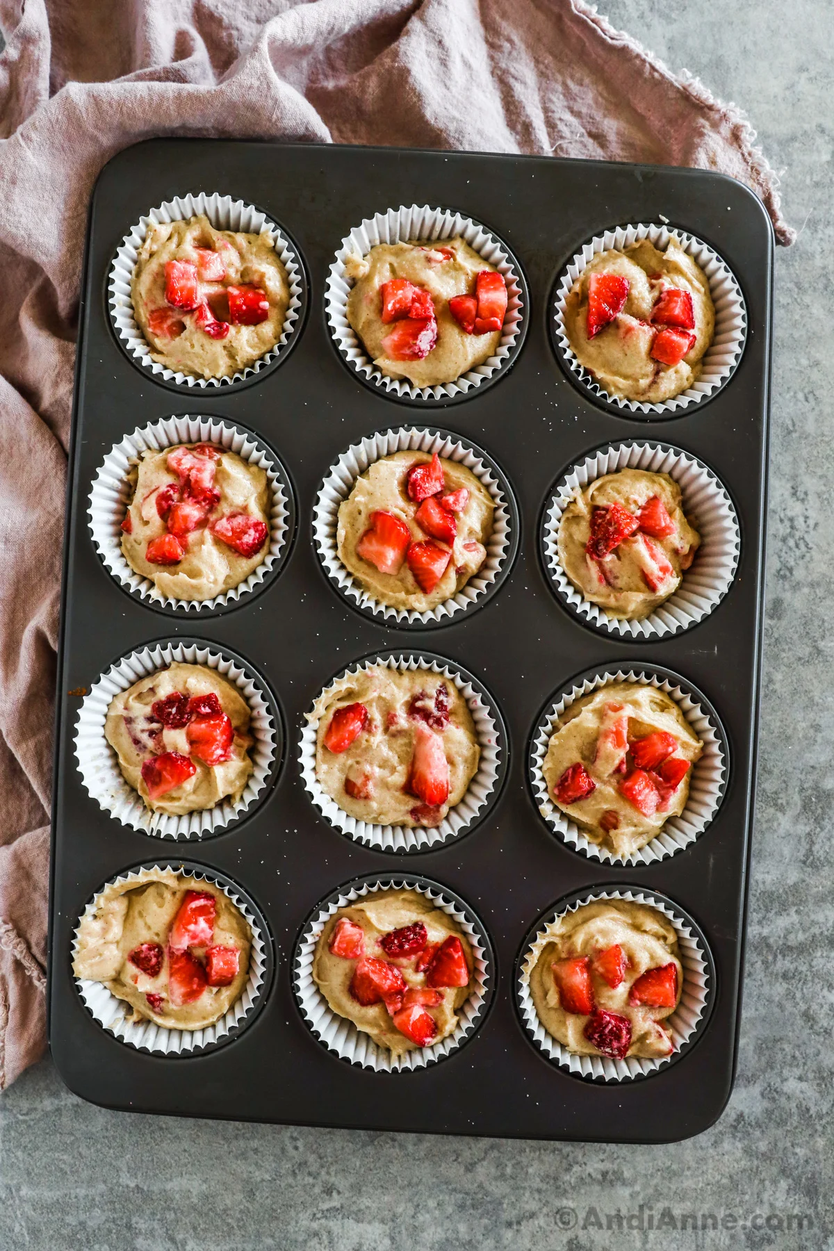 Muffin pan with batter and chopped strawberries in each paper cupcake liner.