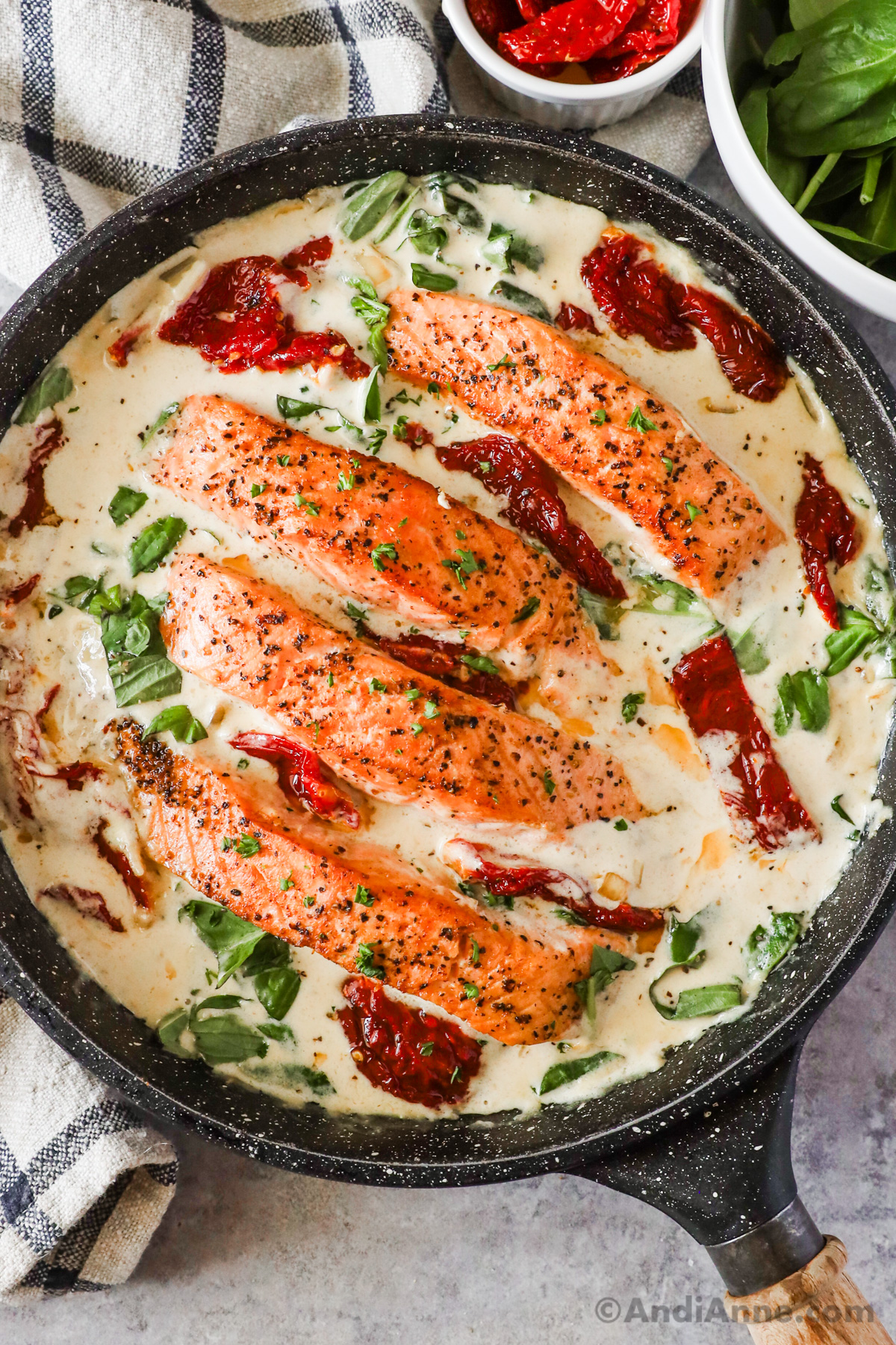 A frying pan with creamy sauce, sun dried tomatoes, basil and salmon fillets.