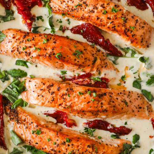 A pan of salmon fillets, sundried tomato and fresh basil in a creamy sauce