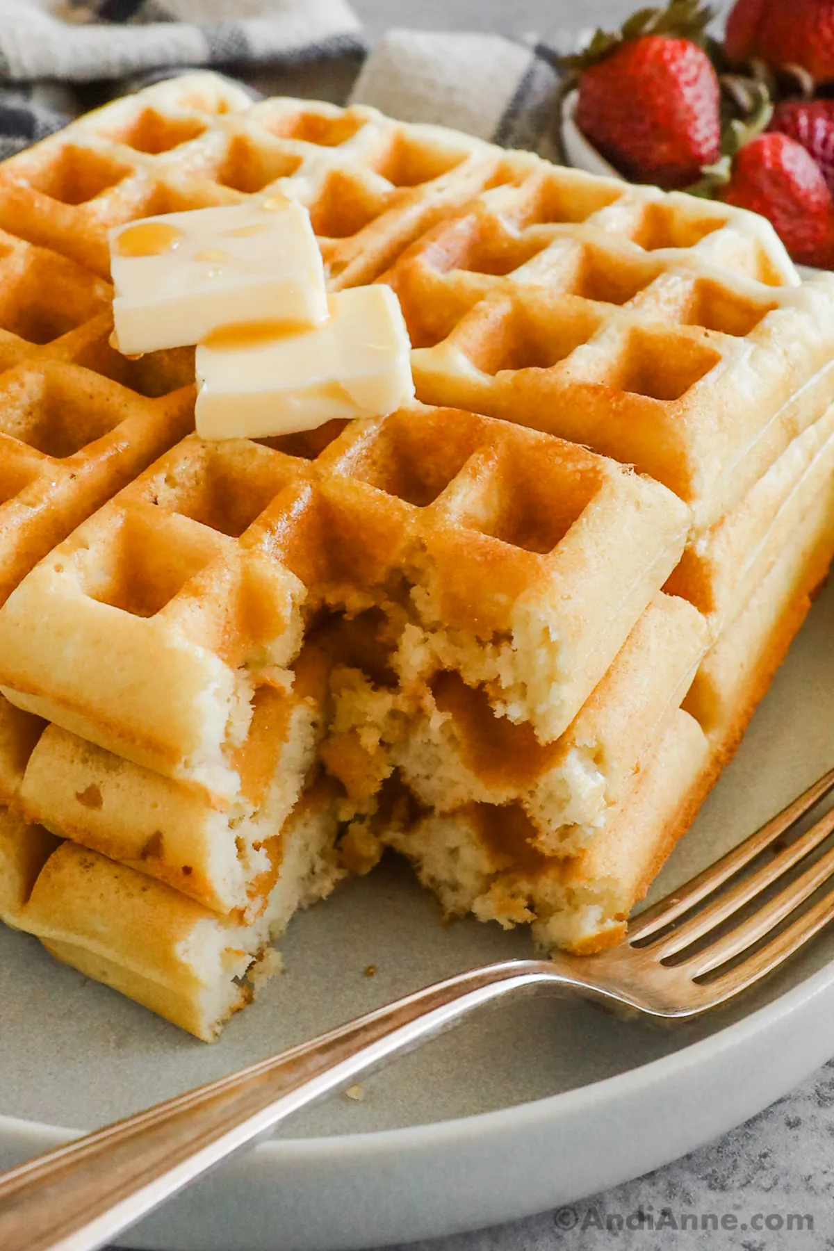 A stack of classic waffles with butter and syrup drizzled on top and forks in the front.