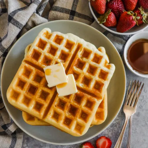 Waffles on a plate with butter, surrounded with berries and syrup.