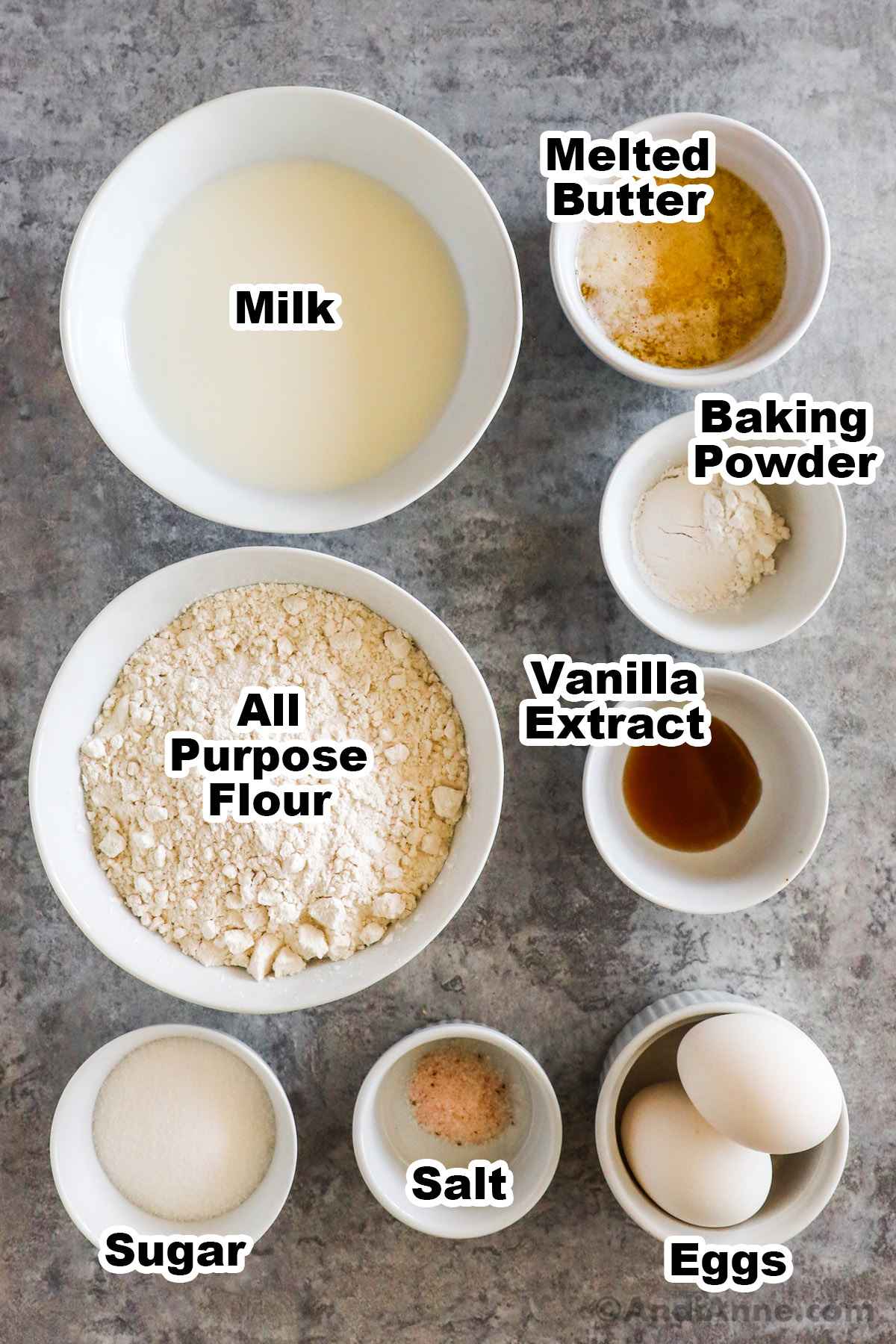 Recipe ingredients on the counter including bowls of milk, melted butter, flour, vanilla, sugar, salt and eggs.