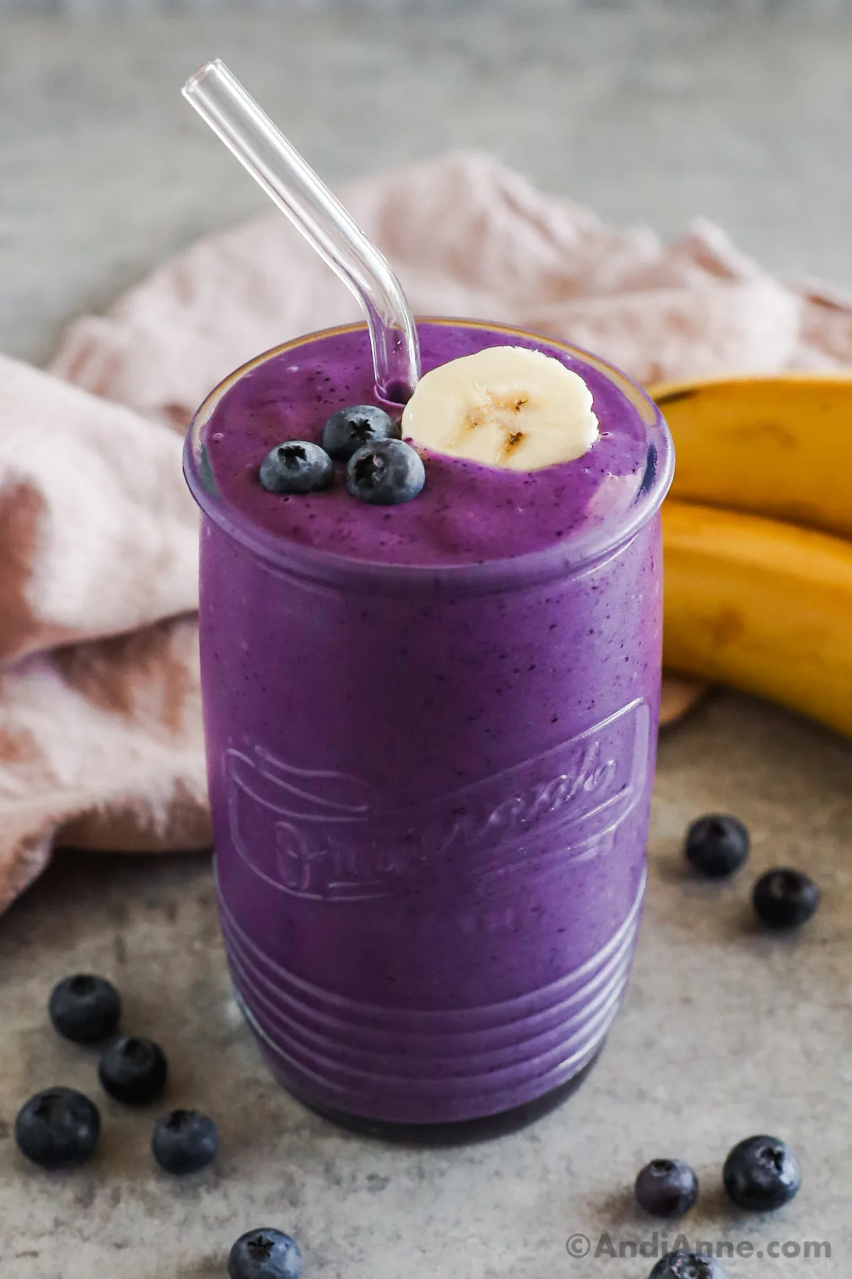 A glass with blueberry smoothie topped with a slice of banana and fresh blueberries