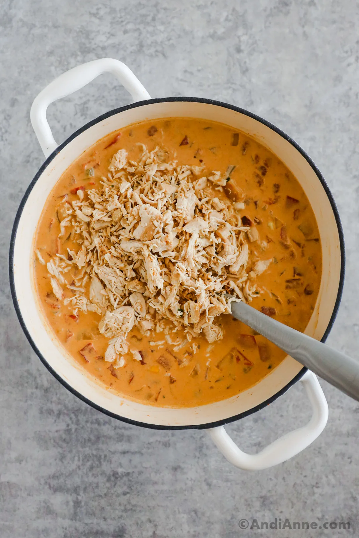 Shredded chicken dumped into a pot of creamy orange colored soup.