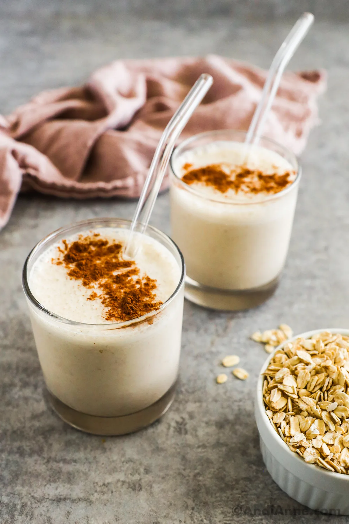 Two glasses of a white smoothie topped with cinnamon and straws.