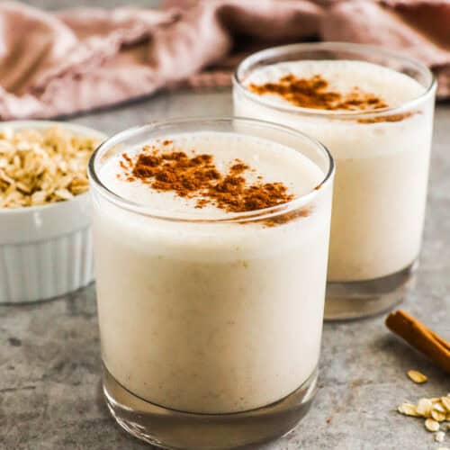 Cups of cinnamon bun breakfast smoothie with cinnamon sprinkled on top.