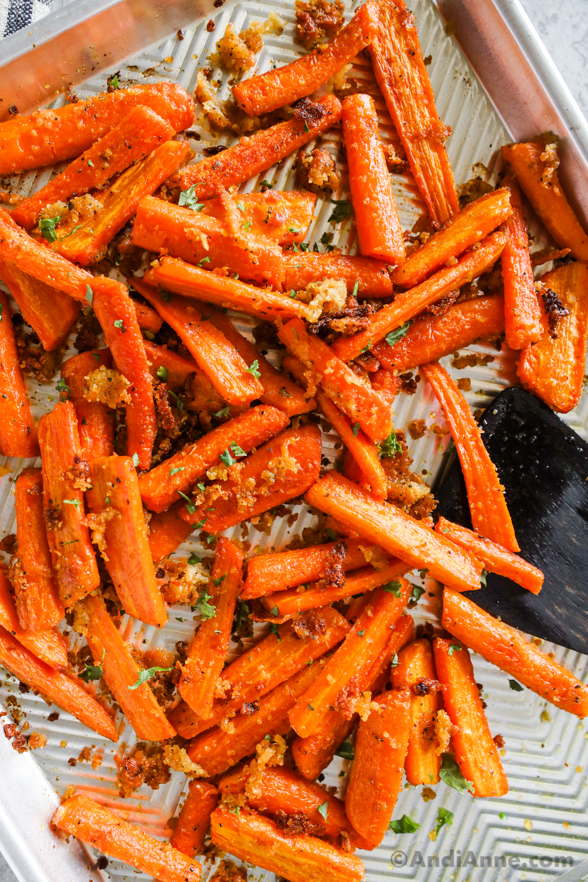 roasted carrots on a baking sheet with a wood spatula.