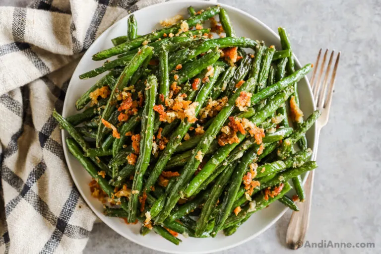 A bowl of green beans with crispy parmesan bread crumb pieces.