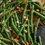 Roasted green beans with parmesan on a baking sheet with a wood spatula.