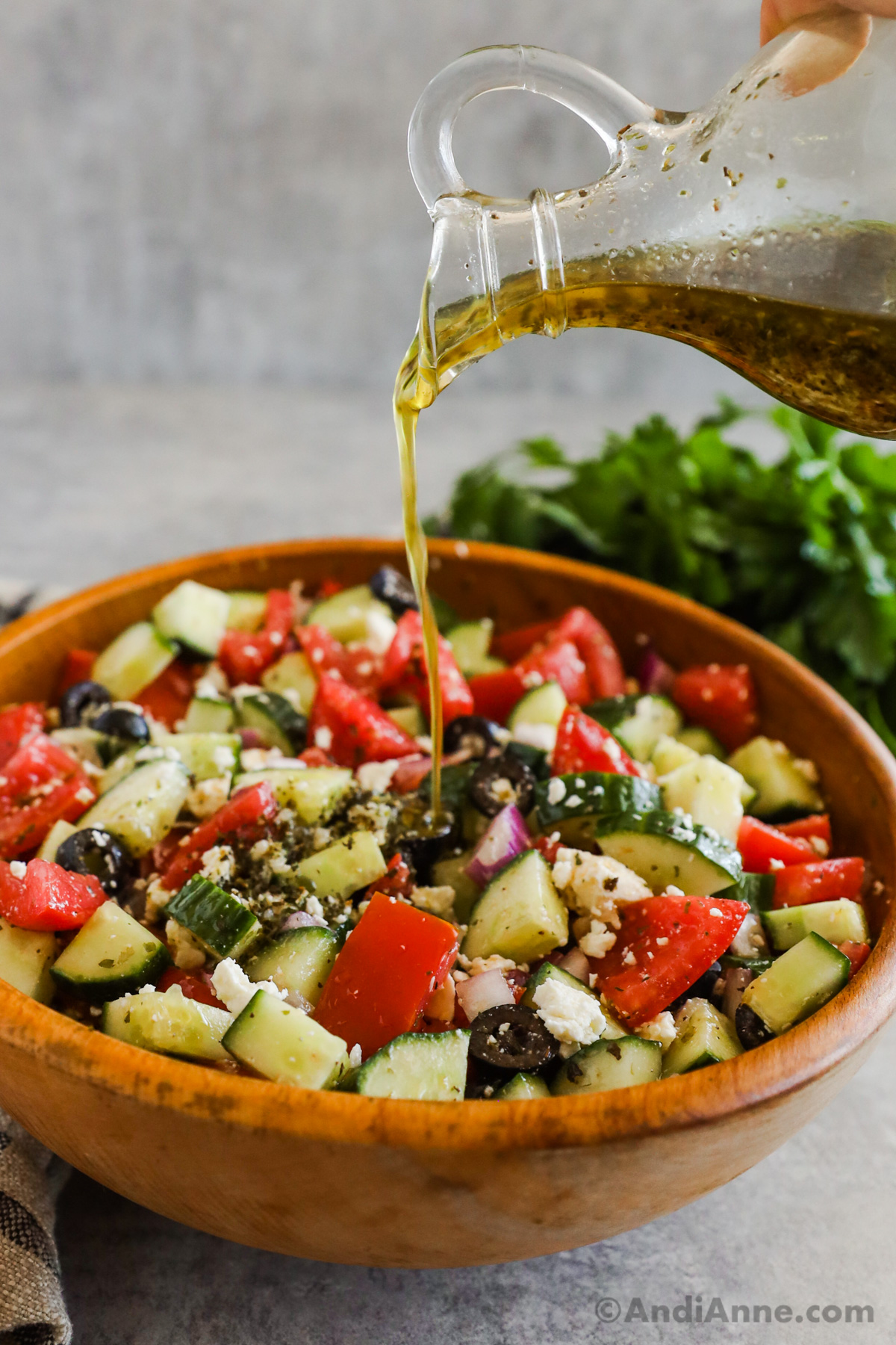 Dressing in a jar being poured overtop of a greek cucumber tomato salad.
