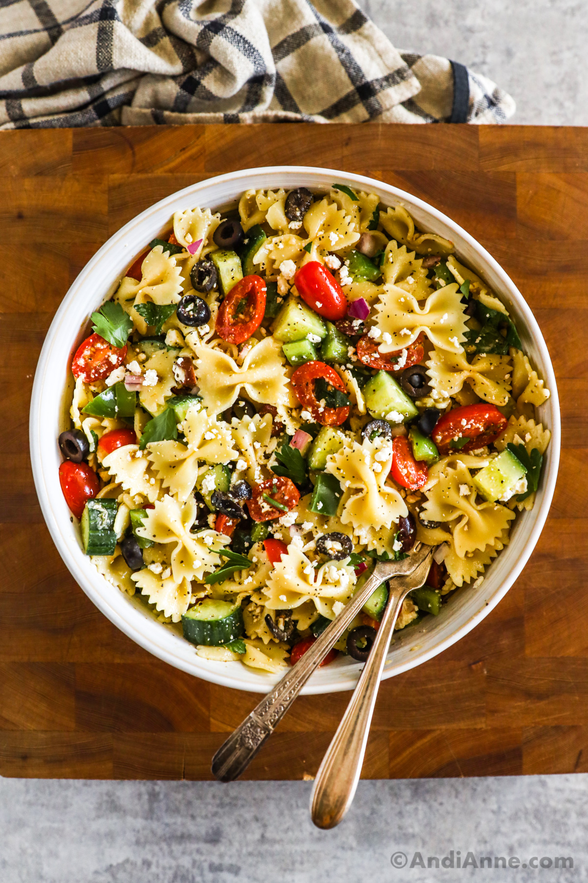 Looking down at a greek pasta salad with farfalle pasta, tomatoes, cucumber, olives and feta cheese.
