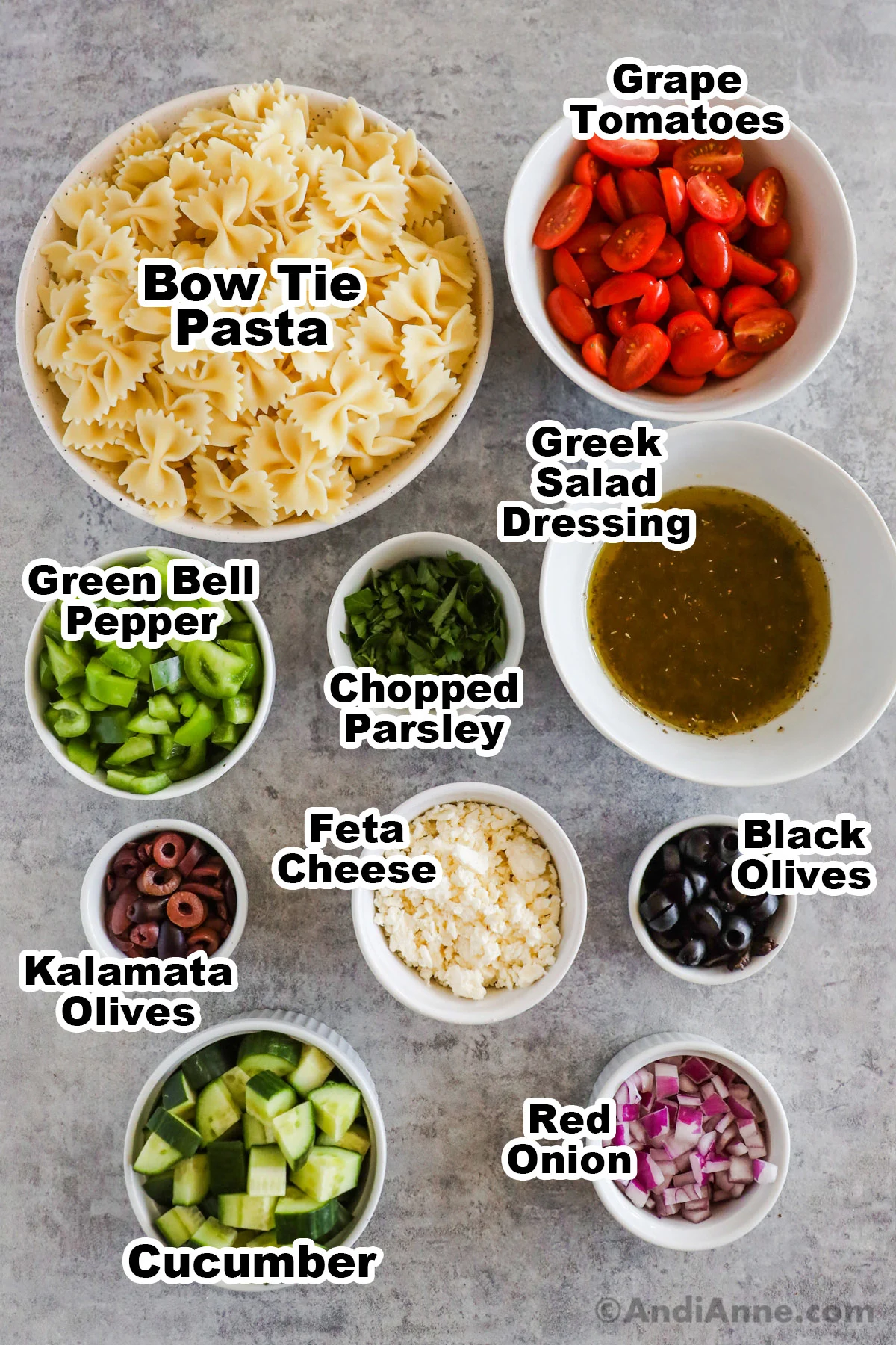 Recipe ingredients in bowls including bowl of farfalle pasta, sliced grape tomatoes, greek salad dressing, chopped parsley, green bell pepper, feta cheese, black olives, kalamata olives, cucumber and red onion.