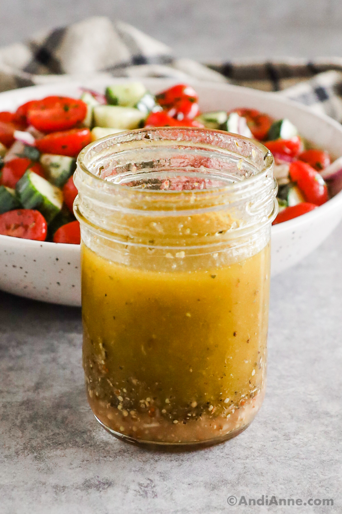 Greek salad dressing recipe in a mason jar with cucumber tomato salad dressing in the background.