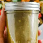 A hand holding a mason jar with greek salad dressing inside.
