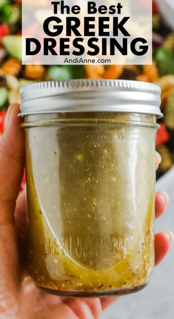 A hand holding a mason jar with greek salad dressing inside.