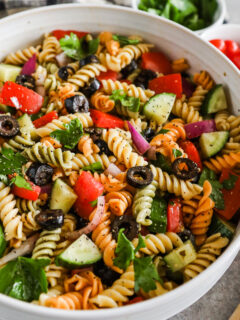 A bowl of italian pasta salad with rotini noodles, tomatoes, cucumbers and olives.