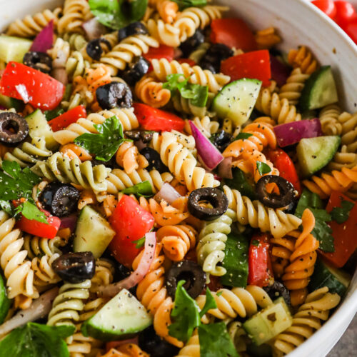 A bowl of italian pasta salad with rotini noodles, tomatoes, cucumbers and olives.